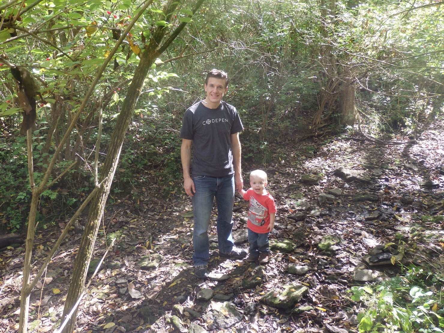 Two year old and dad standing on wet, but not underwater, creek bed rocks