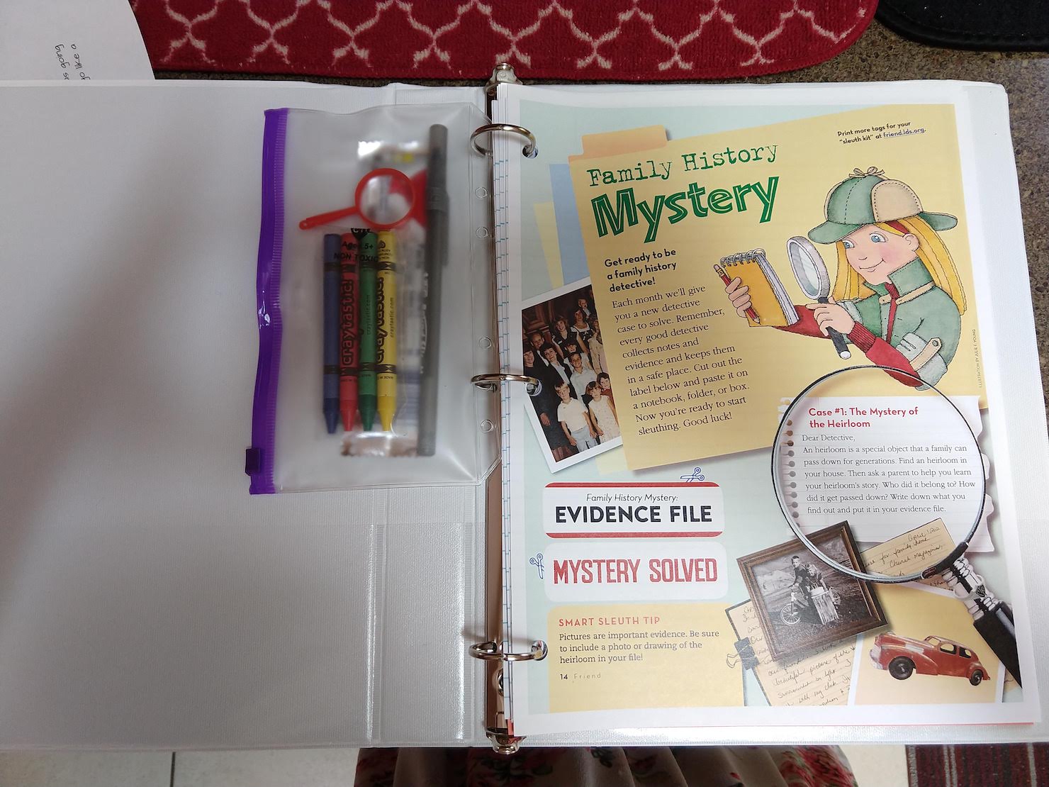 open binder with a supply bag with crayons, a pen, candy, and a toy magnifying glass