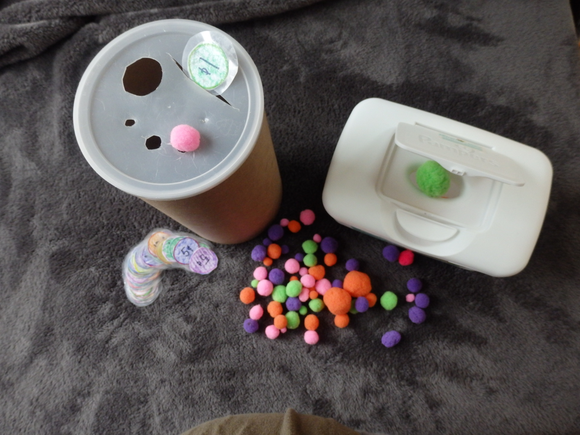 laminated paper coins that fit in slots and pom poms that fit in holes cut in a oats tub