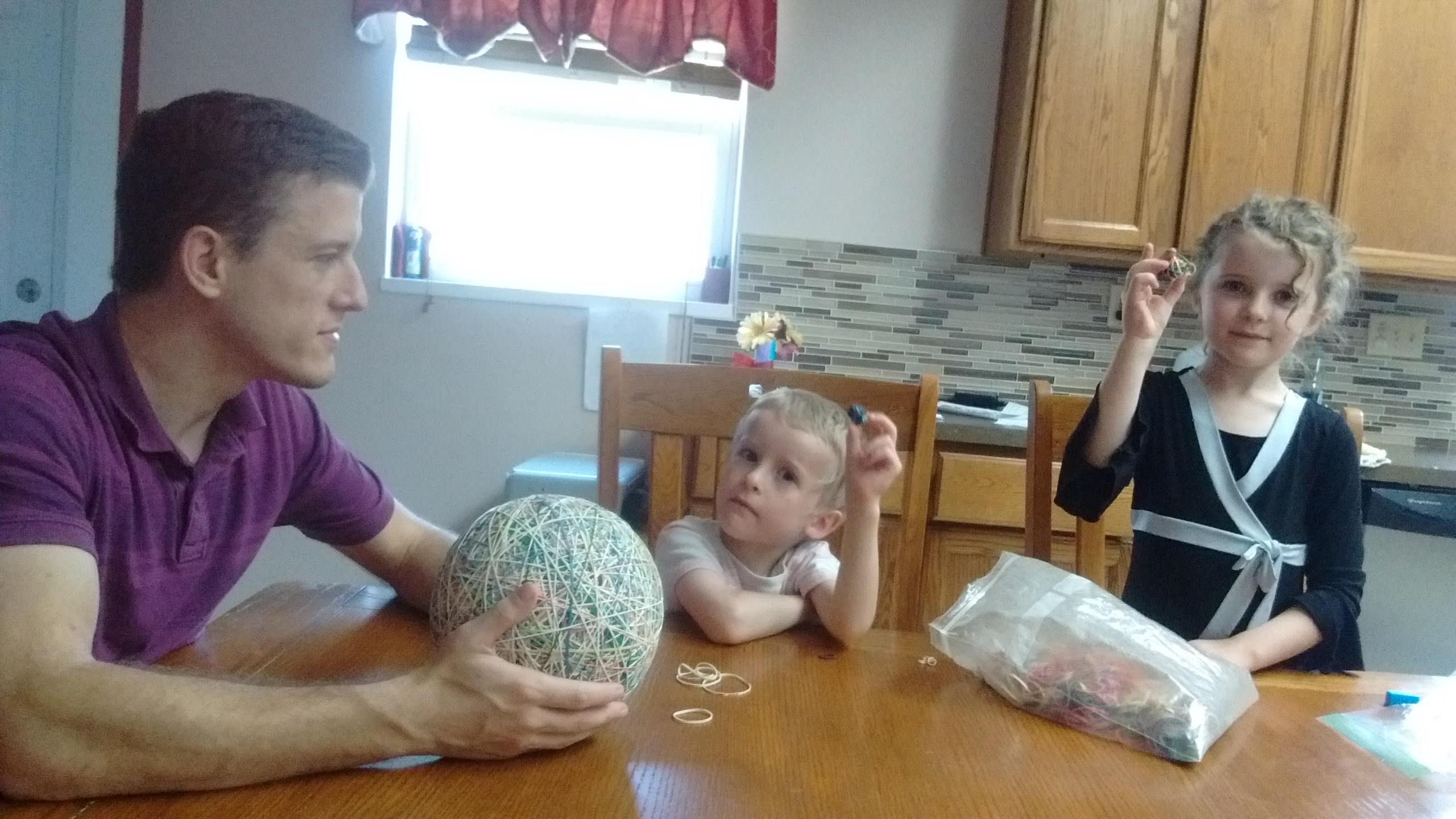 a father showing children how to make rubber band balls