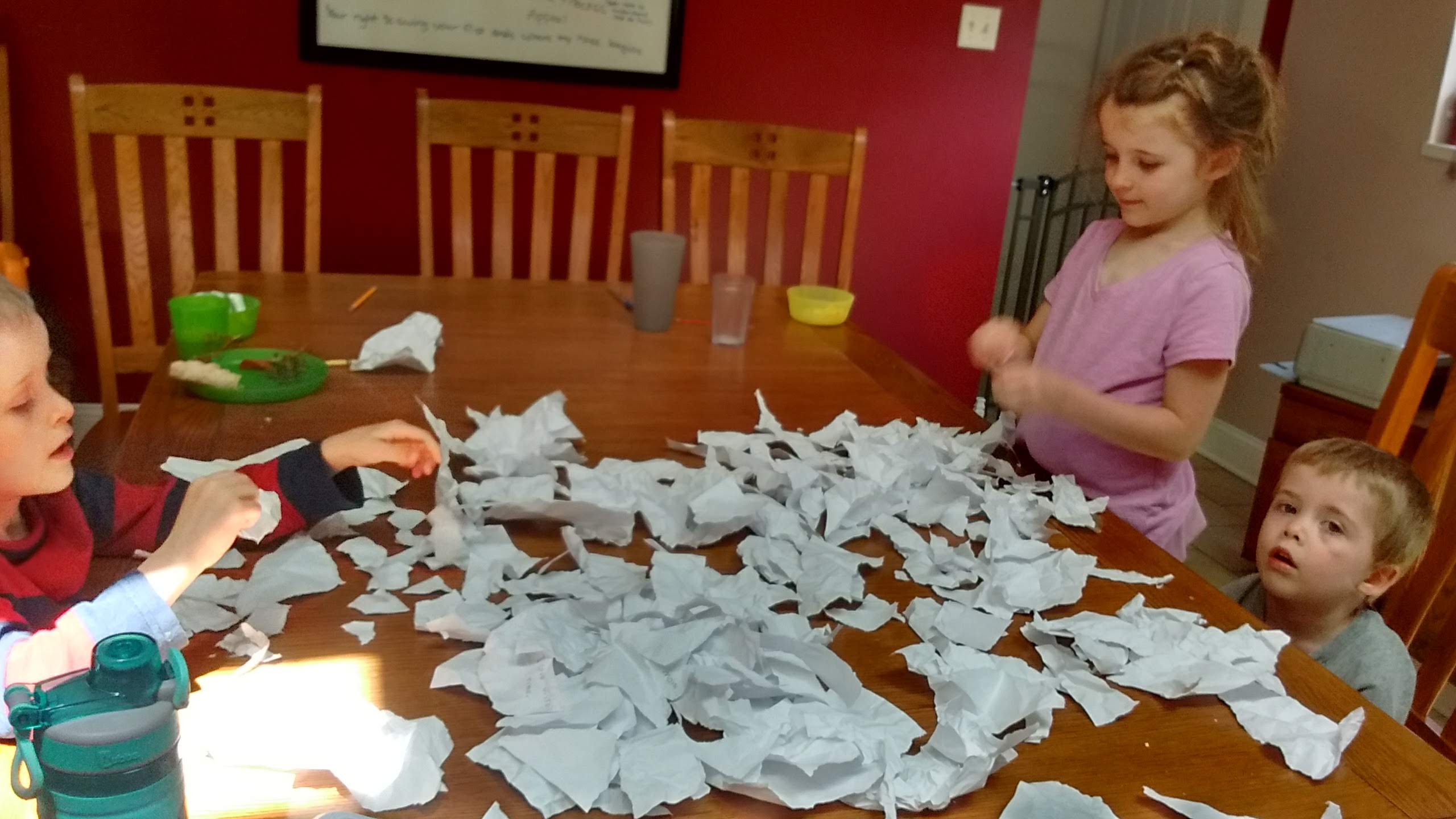 three children tearing up paper in a big pile at the table