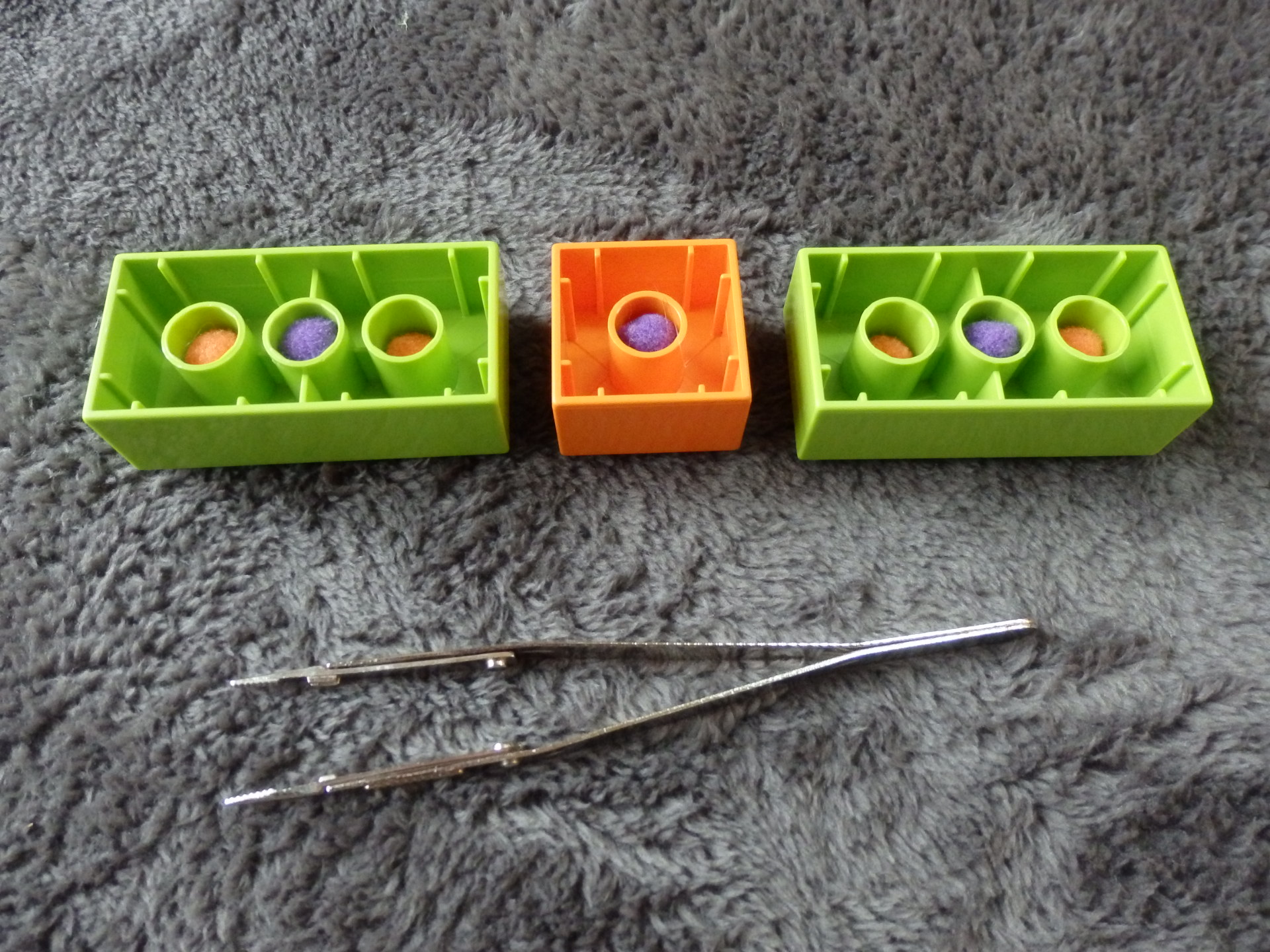 pom poms in the bottom holes of a Duplo with a pair of tweezers