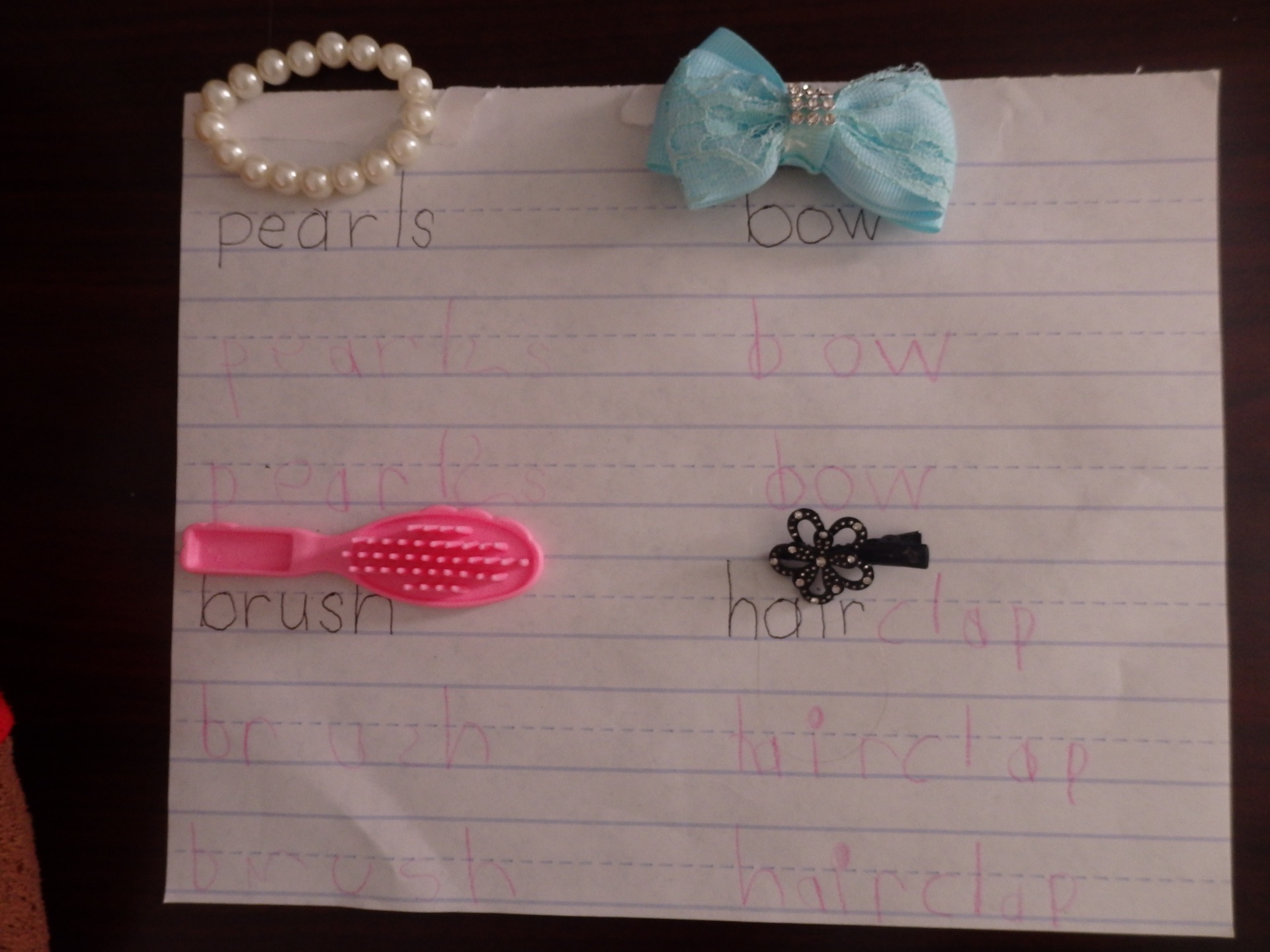 page with girly objects on it, pearls, hair clip, brush, etc, with the words written by an adult and then copied by a child