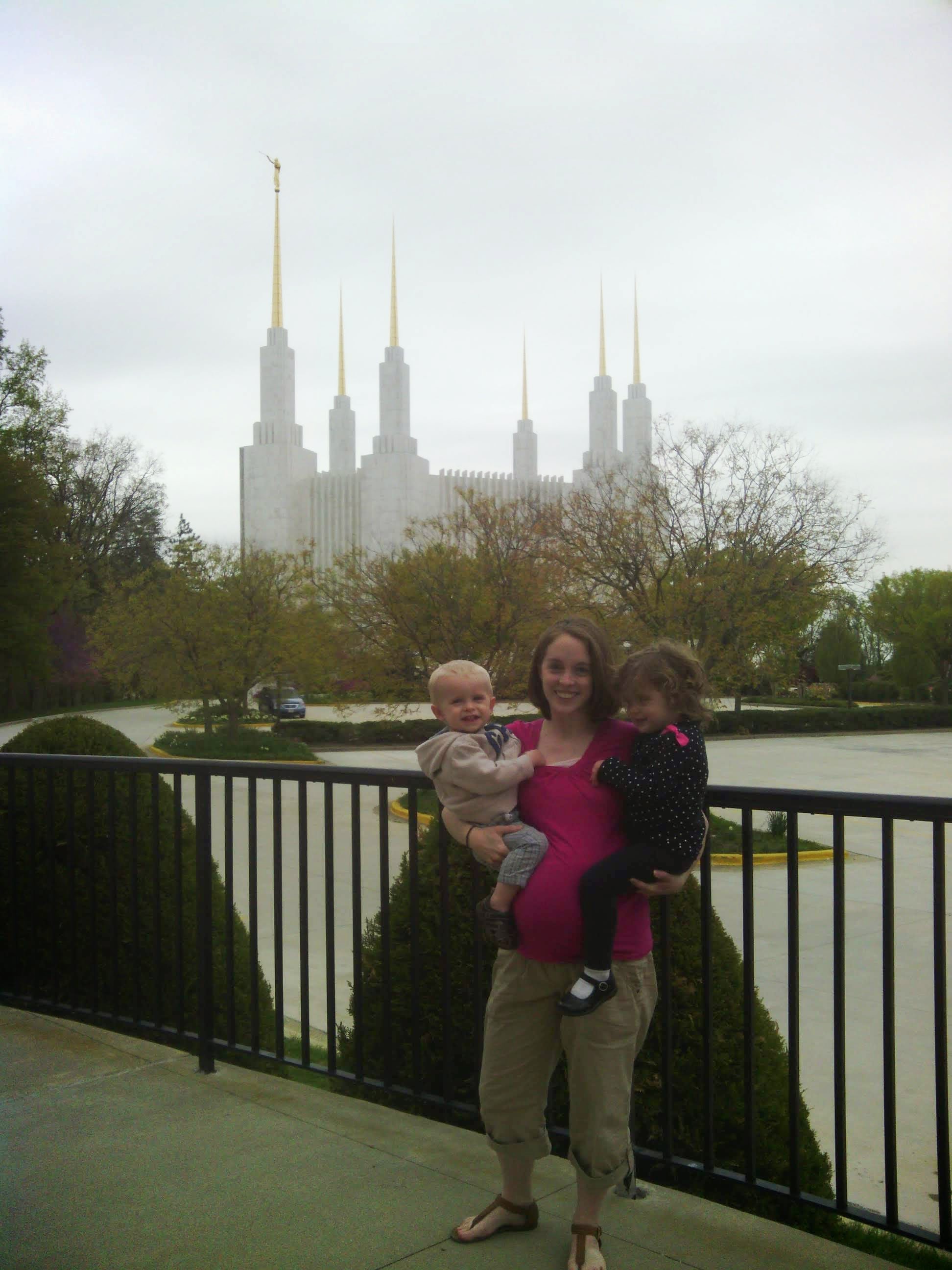 a pregnant woman holding two young children standing in front of the Washington DC temple