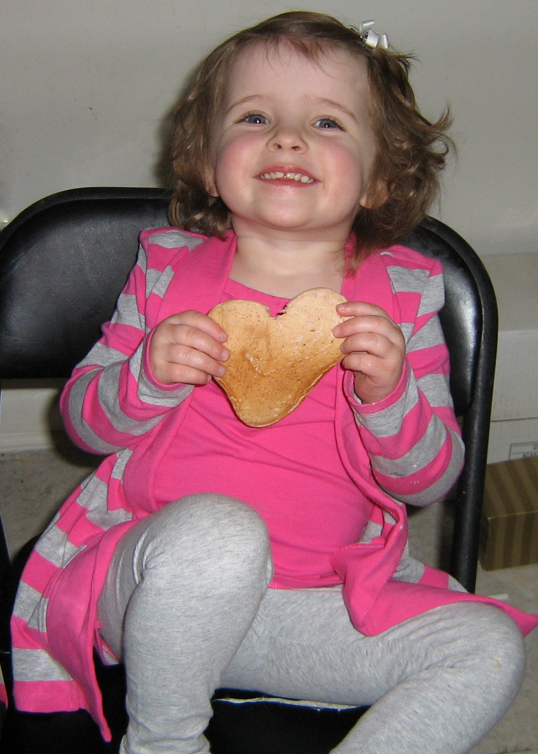 a toddler holding a pancake in the shape of a heart