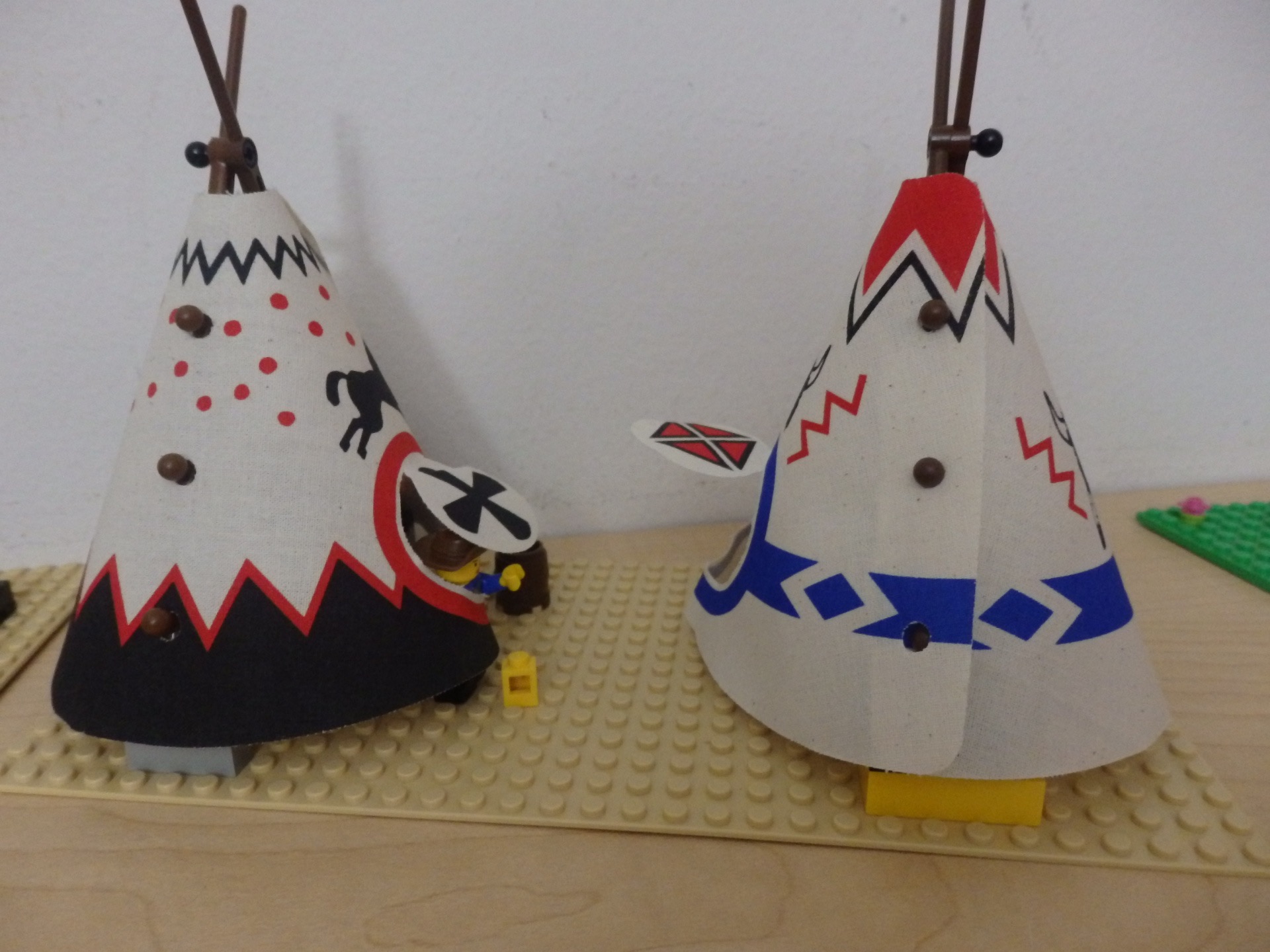 Lego figure sticking out of a teepee, reaching for a yellow block on the ground