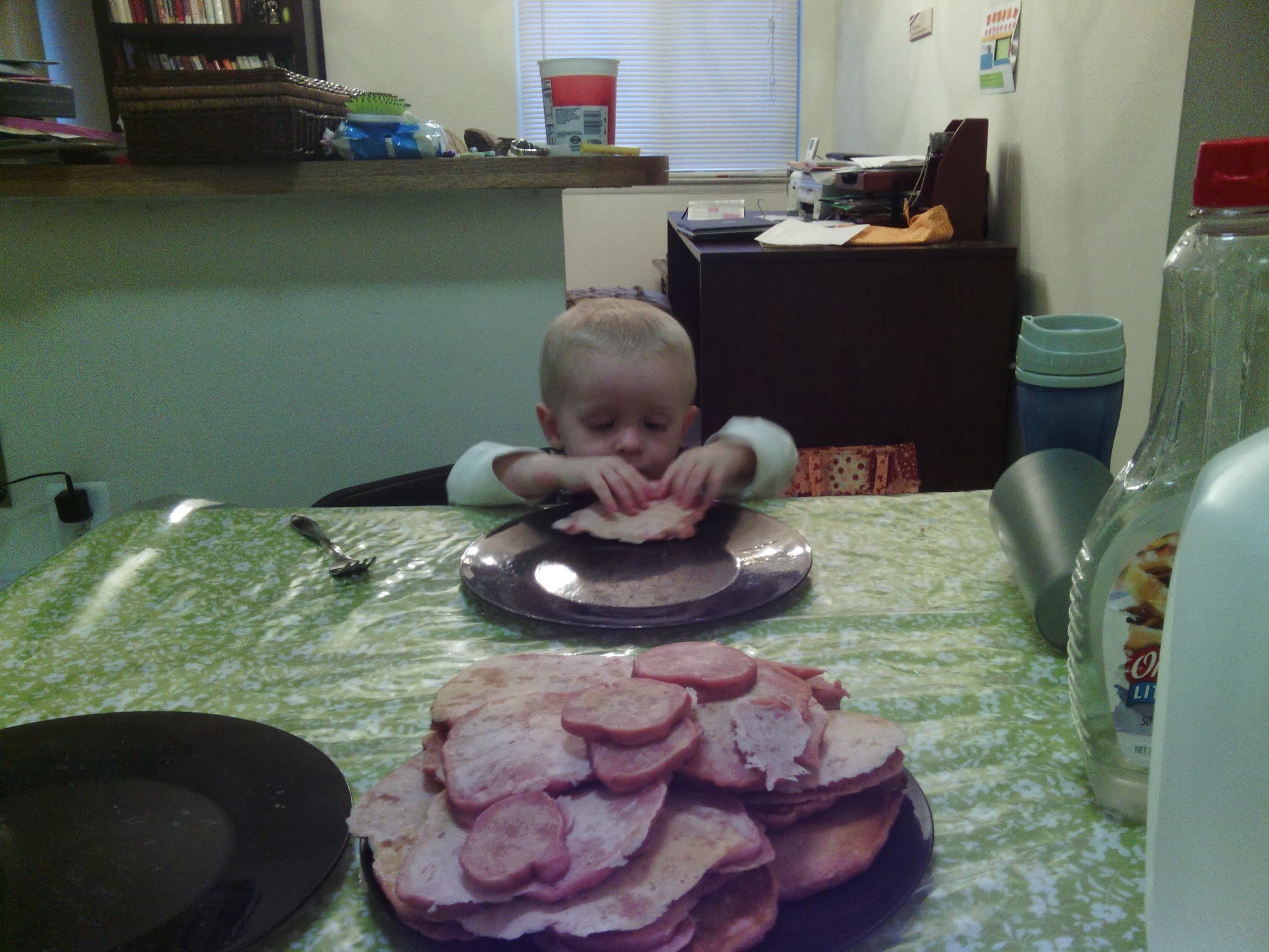 a toddler eating one pancake from a huge pile